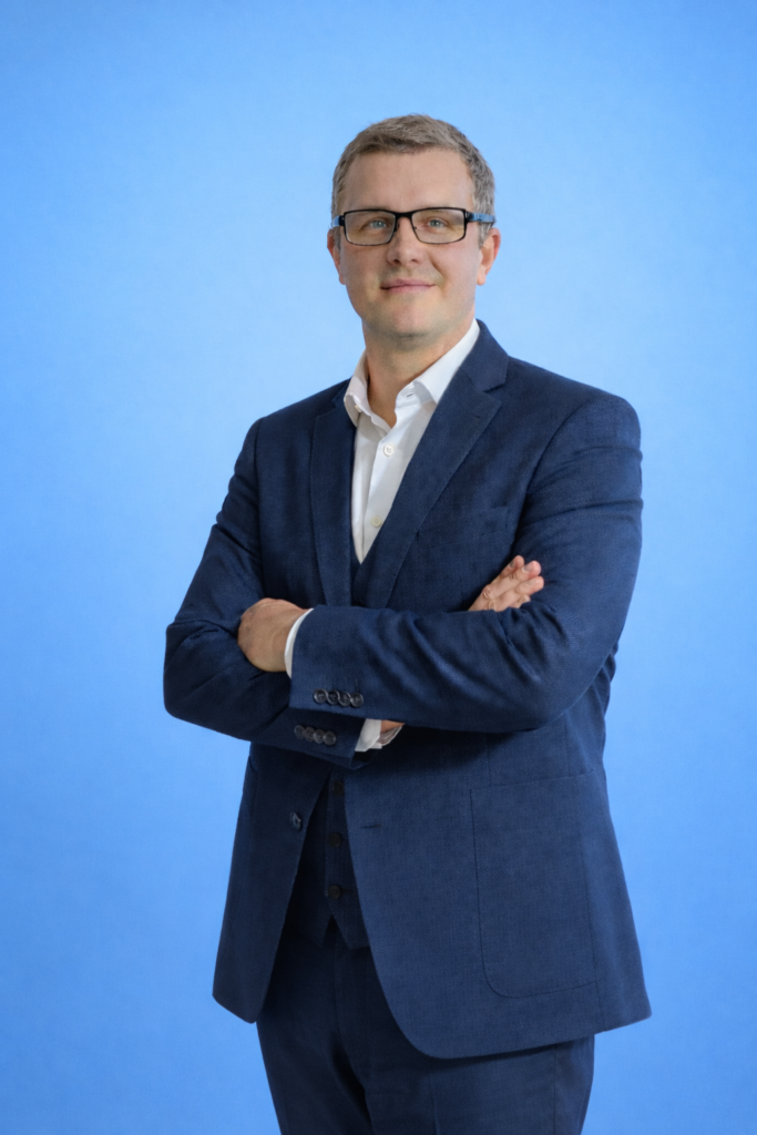 Thomas Dömland stehen in blauer Anzug. Hintergrund hell Blaue. 